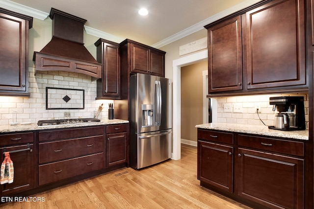 kitchen featuring light stone countertops, ornamental molding, appliances with stainless steel finishes, custom range hood, and light wood-type flooring