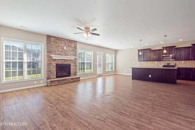 unfurnished living room featuring a stone fireplace, plenty of natural light, and dark hardwood / wood-style flooring