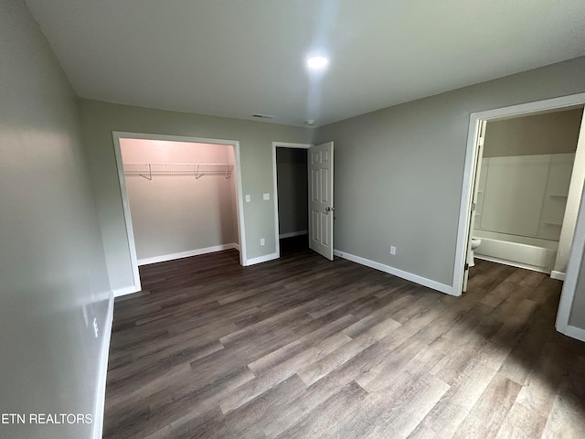 unfurnished bedroom featuring a spacious closet, connected bathroom, dark hardwood / wood-style floors, and a closet