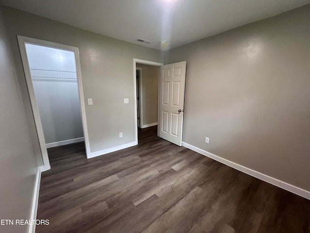 unfurnished bedroom with a closet, a walk in closet, and dark wood-type flooring