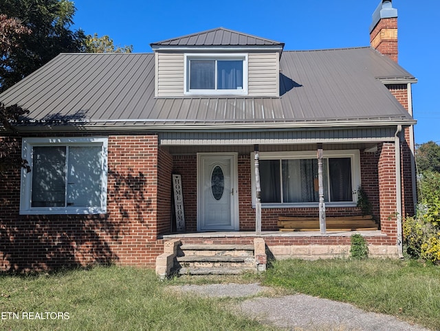 view of front of house featuring a chimney, covered porch, brick siding, and metal roof