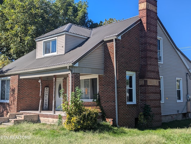 view of front of property with brick siding, covered porch, a chimney, and metal roof