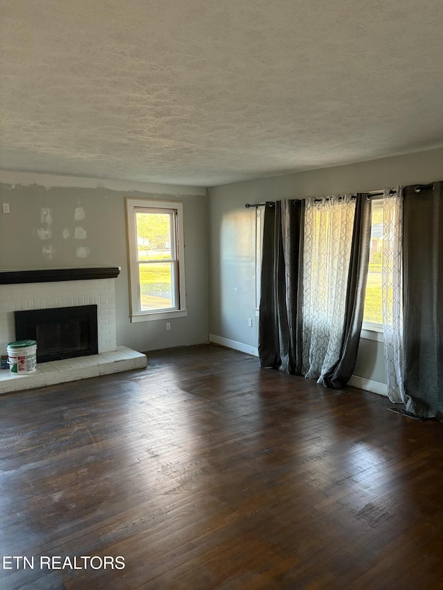 unfurnished living room featuring a fireplace, a textured ceiling, baseboards, and wood finished floors