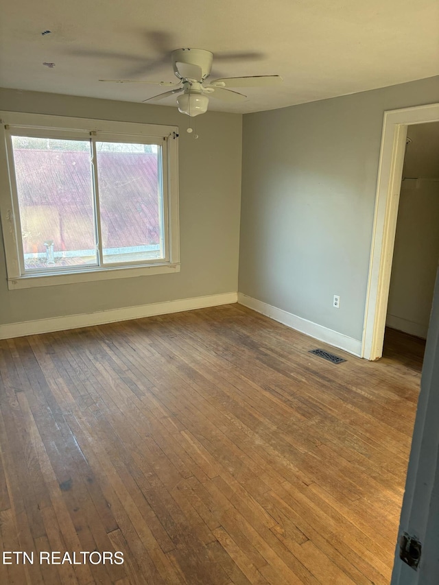 spare room with a ceiling fan, visible vents, baseboards, and wood-type flooring