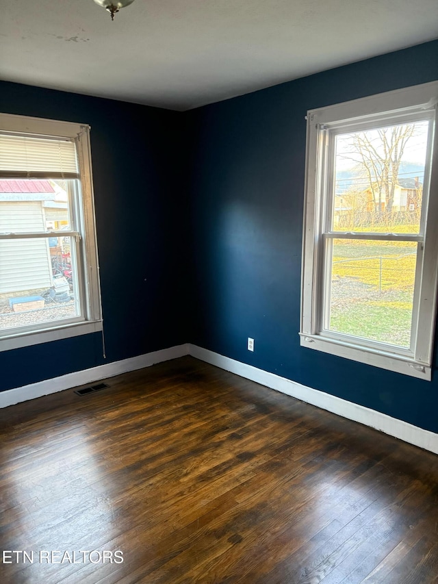 unfurnished room featuring visible vents, baseboards, and dark wood-style flooring