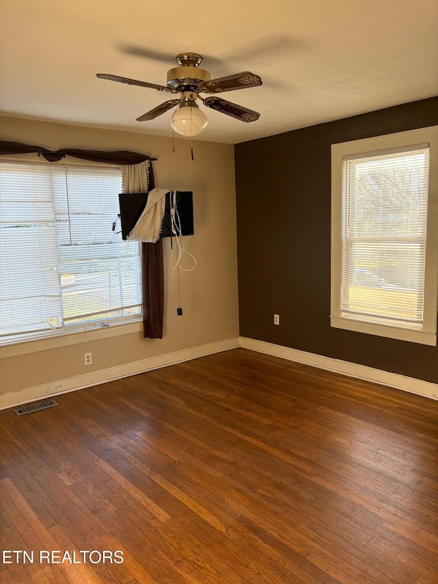 empty room with dark wood finished floors, baseboards, visible vents, and ceiling fan