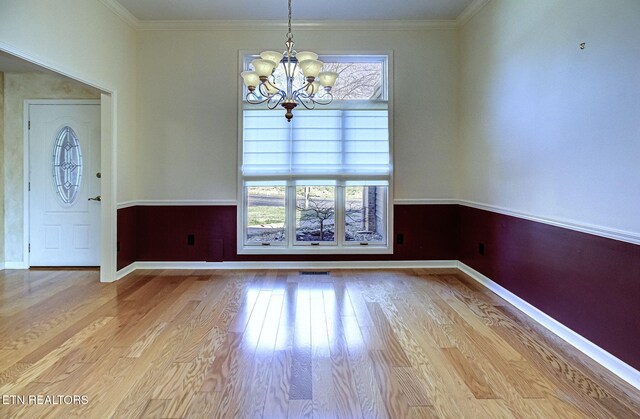 unfurnished dining area with an inviting chandelier, wood finished floors, baseboards, and ornamental molding