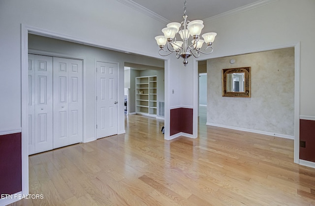 unfurnished dining area with a notable chandelier, built in features, crown molding, light wood finished floors, and baseboards