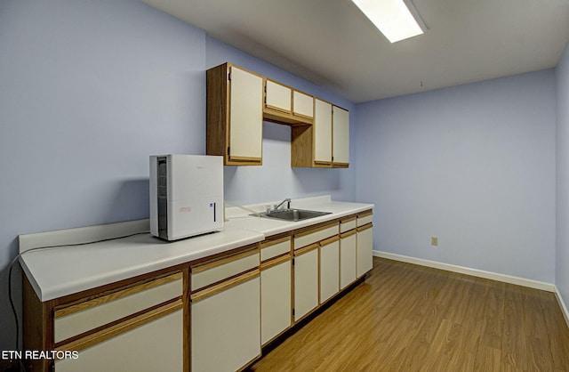 kitchen with baseboards, light countertops, light wood-style floors, and a sink