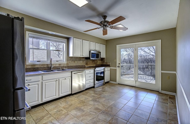 kitchen with a ceiling fan, a sink, backsplash, appliances with stainless steel finishes, and white cabinets