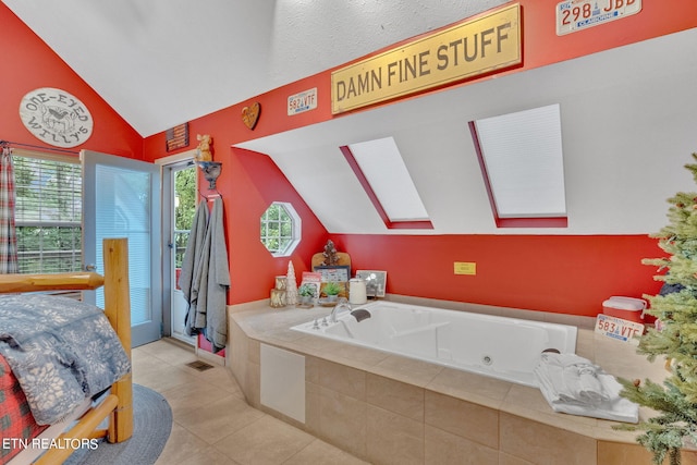 bathroom with vaulted ceiling with skylight, tile patterned flooring, and tiled bath