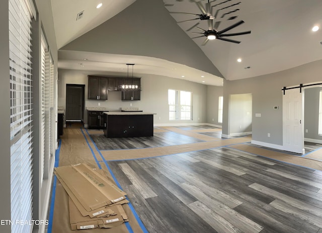 living room featuring a barn door, ceiling fan with notable chandelier, dark wood-type flooring, and high vaulted ceiling