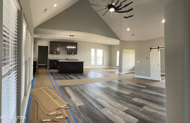 unfurnished living room featuring ceiling fan with notable chandelier, dark hardwood / wood-style floors, a barn door, and high vaulted ceiling