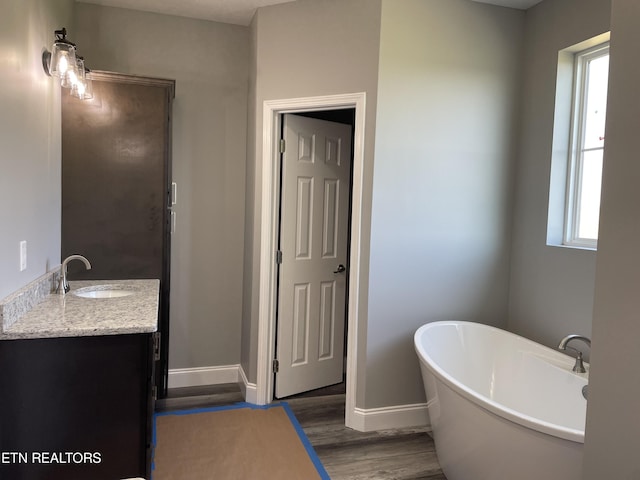 bathroom featuring baseboards, wood finished floors, vanity, and a freestanding bath