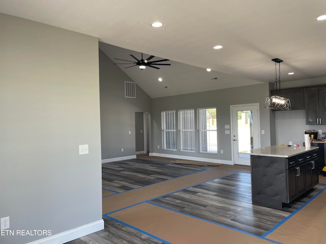 kitchen featuring dark wood-type flooring, hanging light fixtures, a kitchen island, light stone countertops, and ceiling fan