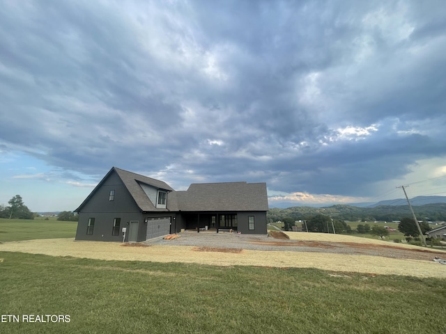 exterior space featuring a shingled roof, a yard, a mountain view, and a garage