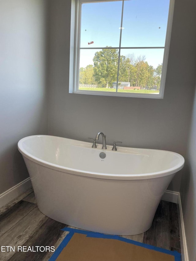 full bath with a freestanding bath, baseboards, and wood finished floors