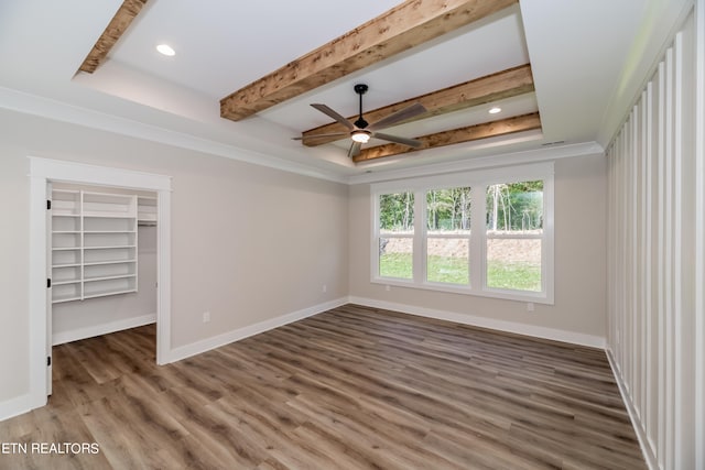 unfurnished bedroom featuring beam ceiling, a spacious closet, baseboards, and wood finished floors