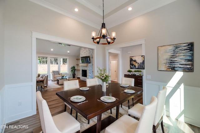 dining space featuring a wainscoted wall, wood finished floors, a fireplace, a decorative wall, and a notable chandelier