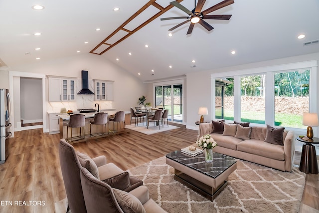 living room featuring high vaulted ceiling, light wood-style flooring, visible vents, and recessed lighting