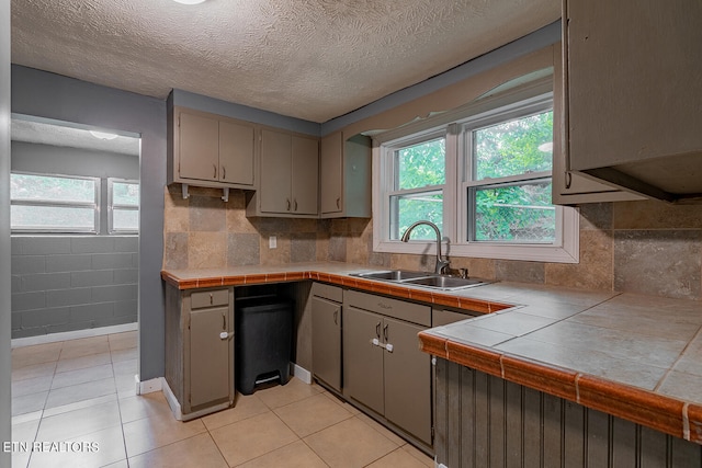 kitchen with gray cabinets, tile countertops, light tile patterned floors, and sink