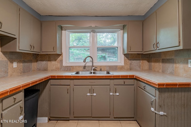 kitchen featuring light tile patterned floors, sink, a textured ceiling, gray cabinets, and tile countertops