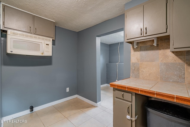 kitchen featuring a textured ceiling, tile countertops, tasteful backsplash, and light tile patterned flooring