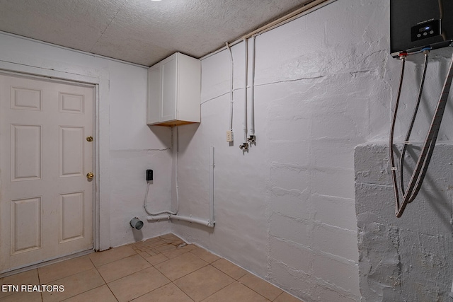 laundry area with a textured ceiling, light tile patterned floors, and cabinets