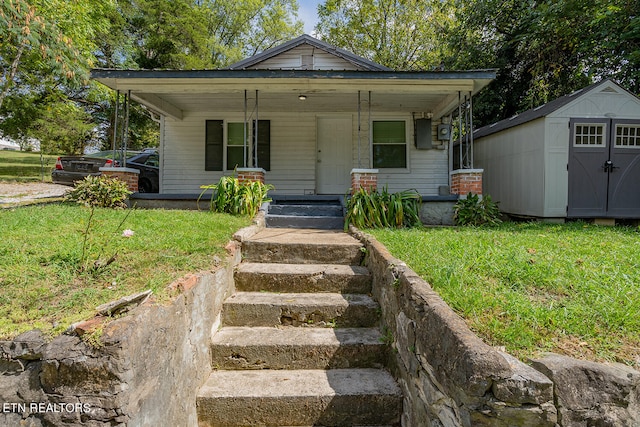 bungalow-style home featuring a front yard, covered porch, and a storage unit