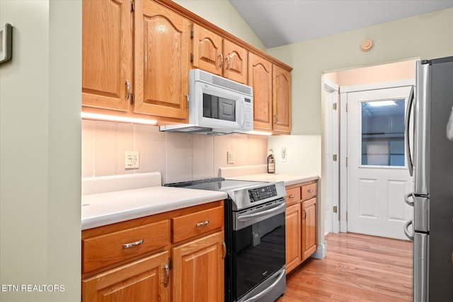 kitchen with decorative backsplash, light wood-type flooring, vaulted ceiling, and stainless steel appliances