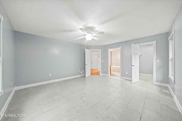 unfurnished bedroom featuring ensuite bath, ceiling fan, a textured ceiling, a spacious closet, and a closet