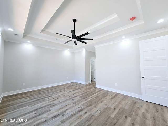 empty room featuring visible vents, a raised ceiling, light wood-style floors, and ornamental molding