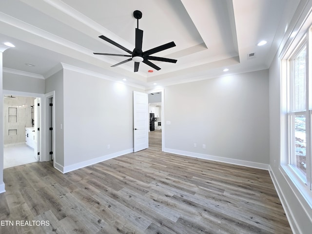 unfurnished room with plenty of natural light, ornamental molding, a tray ceiling, and wood finished floors