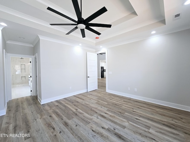 unfurnished bedroom with a tray ceiling, wood finished floors, visible vents, and baseboards