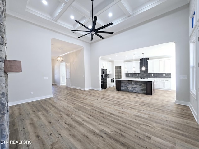 unfurnished living room featuring light wood finished floors, a high ceiling, a ceiling fan, and a sink