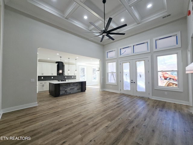 unfurnished living room with visible vents, a sink, coffered ceiling, baseboards, and a towering ceiling