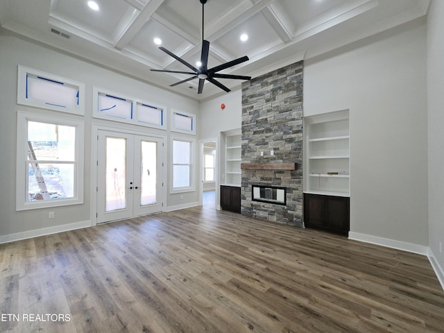 unfurnished living room featuring wood finished floors, baseboards, coffered ceiling, a stone fireplace, and french doors