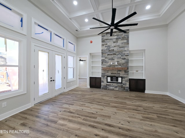 unfurnished living room featuring coffered ceiling, wood finished floors, french doors, a high ceiling, and a stone fireplace