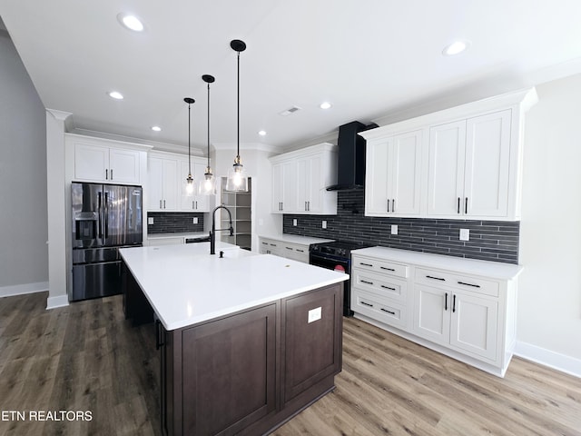 kitchen with a sink, black appliances, light countertops, wall chimney exhaust hood, and light wood-type flooring