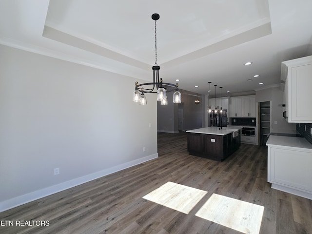 kitchen featuring a tray ceiling, a kitchen island with sink, a chandelier, and oven