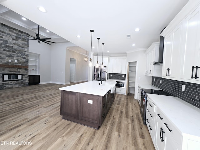 kitchen featuring wall chimney range hood, light wood-type flooring, appliances with stainless steel finishes, a fireplace, and white cabinets