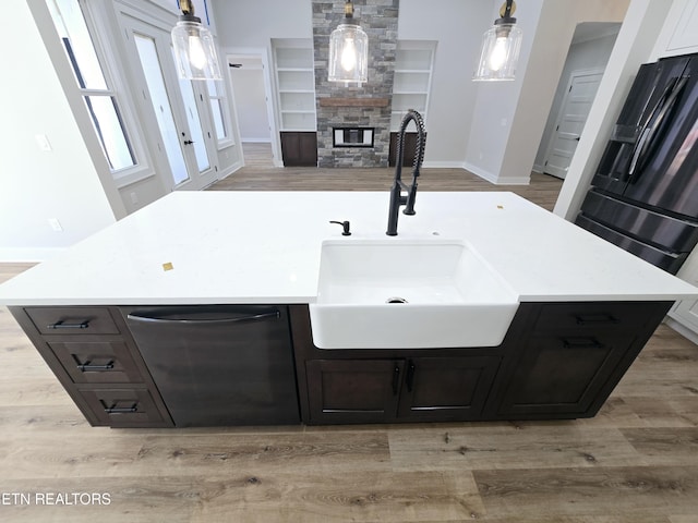 kitchen with light wood finished floors, a sink, a stone fireplace, light countertops, and dishwasher