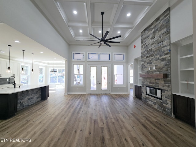 living area featuring a wealth of natural light, a stone fireplace, french doors, wood finished floors, and coffered ceiling