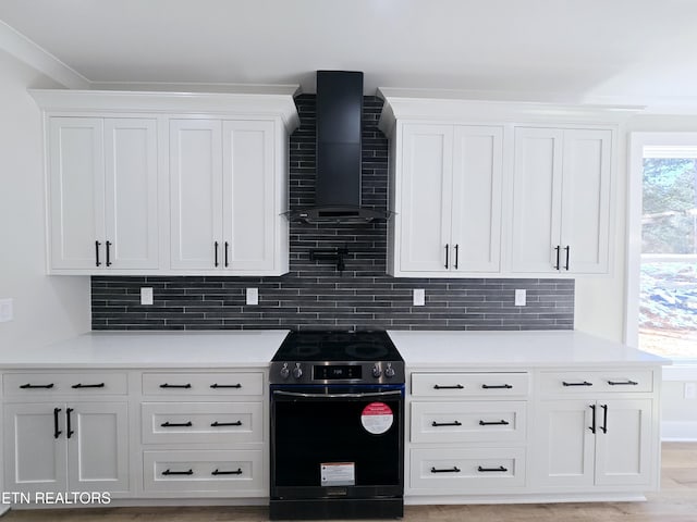 kitchen with decorative backsplash, white cabinetry, stainless steel electric range oven, and wall chimney range hood