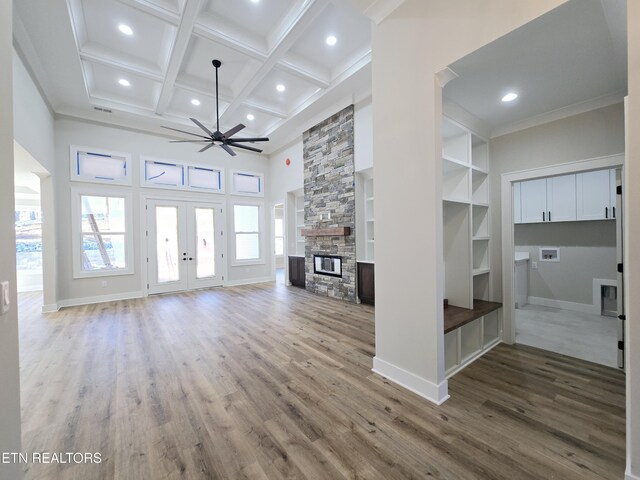 unfurnished living room featuring ceiling fan, beamed ceiling, a fireplace, wood finished floors, and coffered ceiling