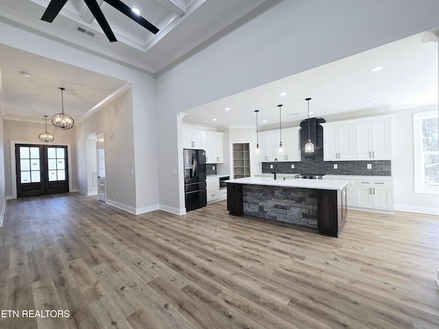 kitchen featuring visible vents, light countertops, decorative backsplash, black refrigerator with ice dispenser, and wall chimney exhaust hood