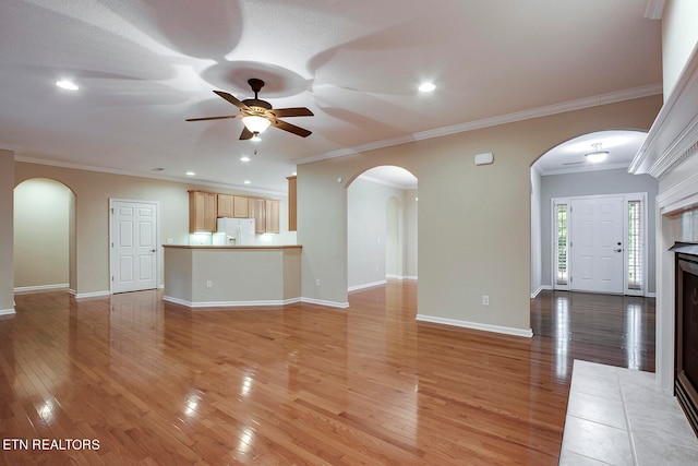 unfurnished living room with ceiling fan, light hardwood / wood-style flooring, a tiled fireplace, and ornamental molding