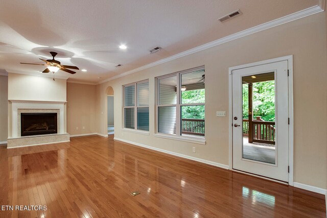 unfurnished living room featuring wood-type flooring, a fireplace, crown molding, and ceiling fan