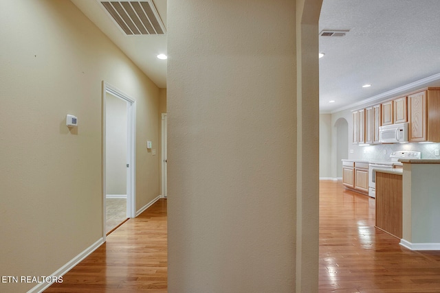 hall featuring a textured ceiling, crown molding, and light hardwood / wood-style floors