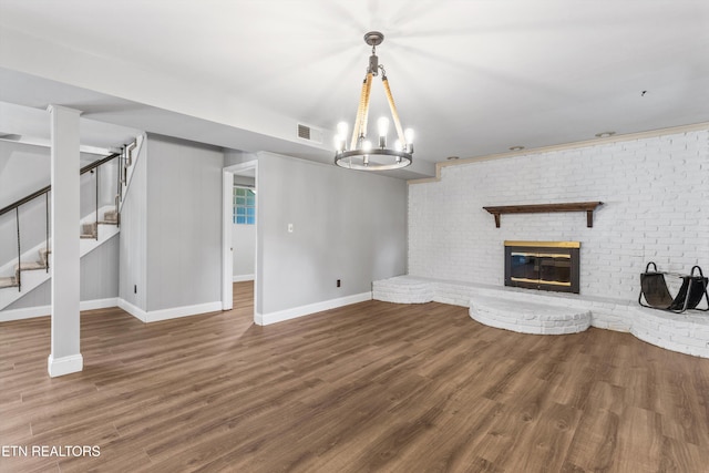 unfurnished living room with a brick fireplace, an inviting chandelier, and hardwood / wood-style floors